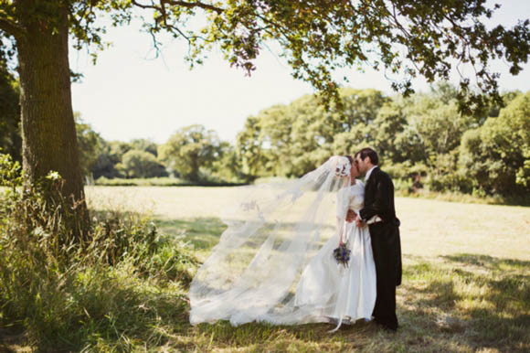 A beautiful bride in her 1950s wedding dress tieing the knot rustic style on a Cornfield on her home farm in Somerset