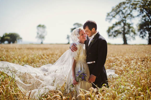A beautiful bride in her 1950s wedding dress tieing the knot rustic style on a Cornfield on her home farm in Somerset